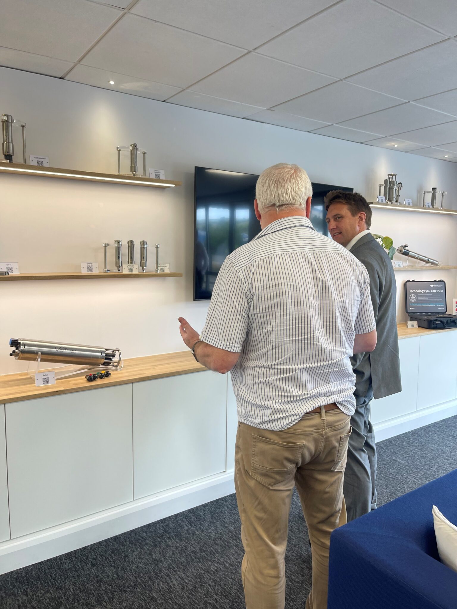 A member of the Devon and Torbay Combined County Authority is being spoken to by a person from Teledyne Valeport. The pair are stood in front of a set of shelves that house different engineering equipment from Teledyne Valeport.