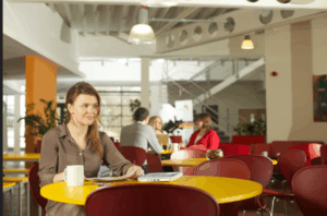 Young woman sat at a table in a social area of a work place