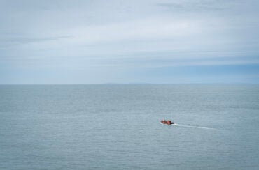 A single boat is travelling on the sea towards the horizon
