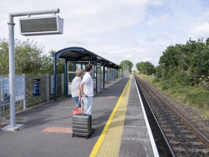 A man waits at a train station holding a suitcase