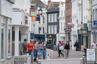 A busy pedestrian street lined with shops and businesses in a historic town center.