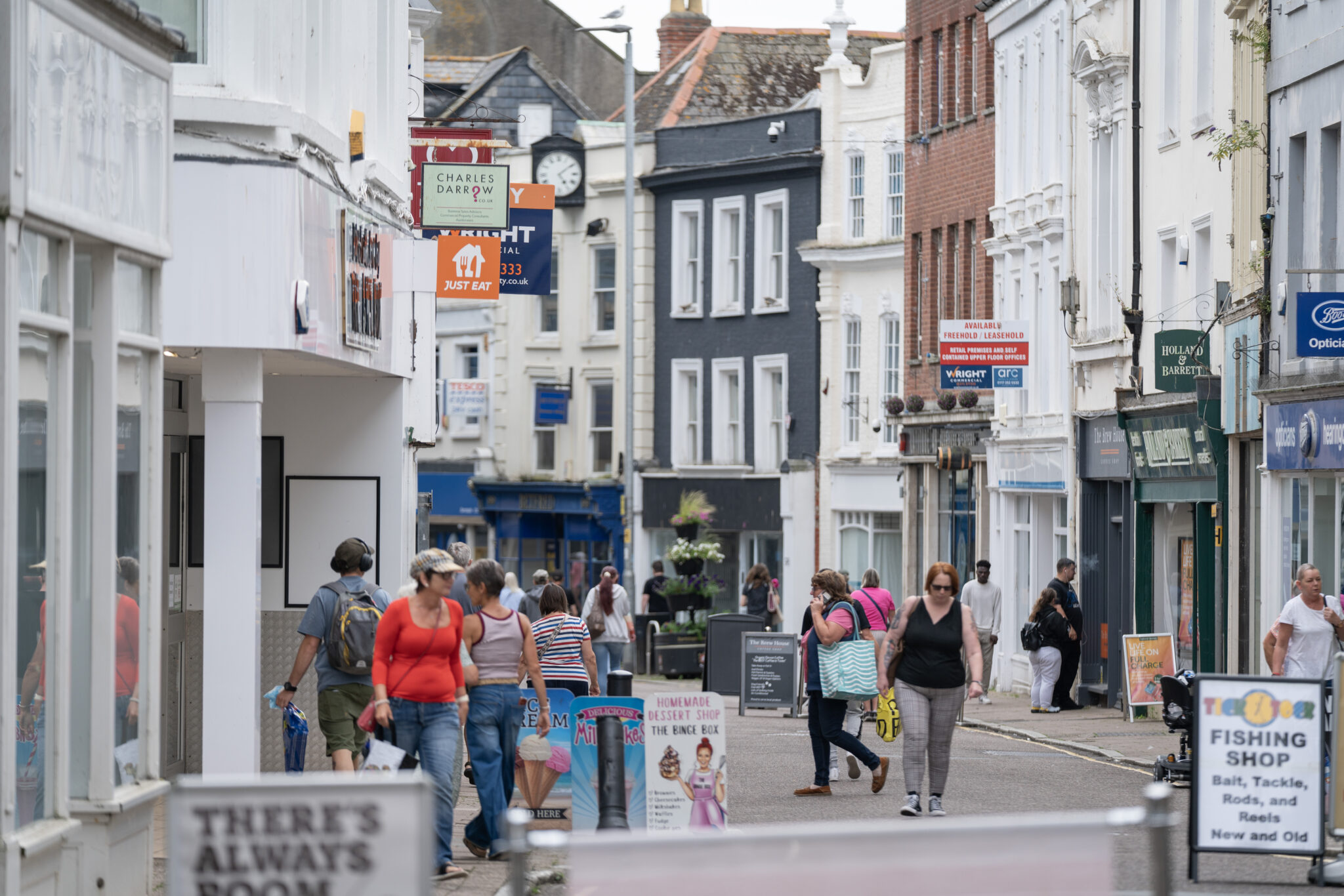 A busy pedestrian street lined with shops and businesses in a historic town center.