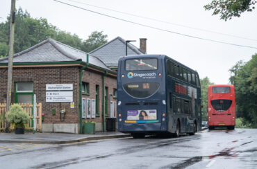 Two buses outside of a train station driving into the distance